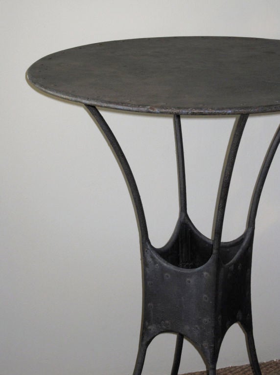 An iron table with dark charcoal patina,<br />
in the style of Giacometti.<br />
France, first-half twentieth century.<br />
Round form metal top<br />
mounted on bent iron base,<br />
web band at center <br />
and flares outward<br />
at