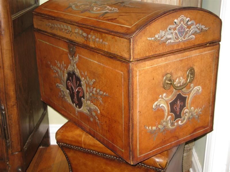 This handsome chest is decorated with a Fleur de Lis design on three sides and on two sides of the lid.  An unusual family crest is depicted on the top of this chest.  The leather is a warm caramel color.  The inside is lined with vintage paper.