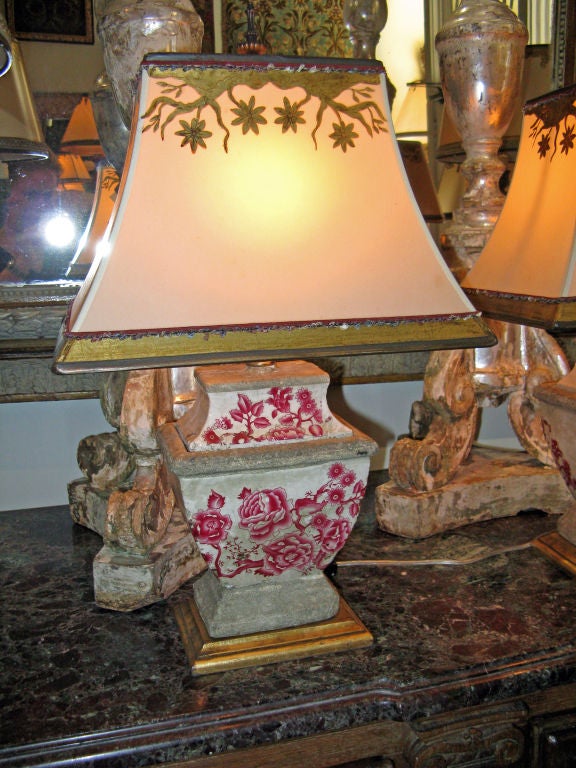 Pair of stoneware urns that have been french mounted into charming lamps.  The custom painted shades have gold leaf detailing that depict the design from the lamps. The red chinoiserie flowers will be a great accent color in any room.
