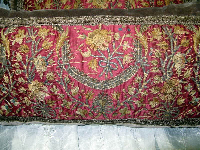 This pair of kidney pillows is designed with antique metallic and silk embroidery on a cranberry silk background. Surrounding this is a metallic gunmetal gray gimp on silk velvet. The backing is diminutive stripes of gray. The tassels are various