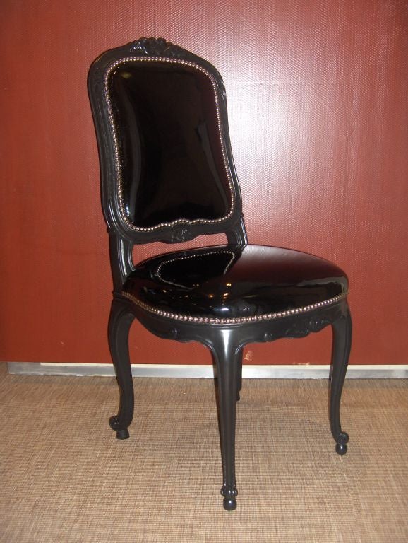 Rococco / Lous XV style carved French side chair with a beautiful curvilinear form. Particularly notable is the curved cabriole leg with a scroll foot over which rests a rounded seat. The frame has been upholstered in a shiny black faux Patent