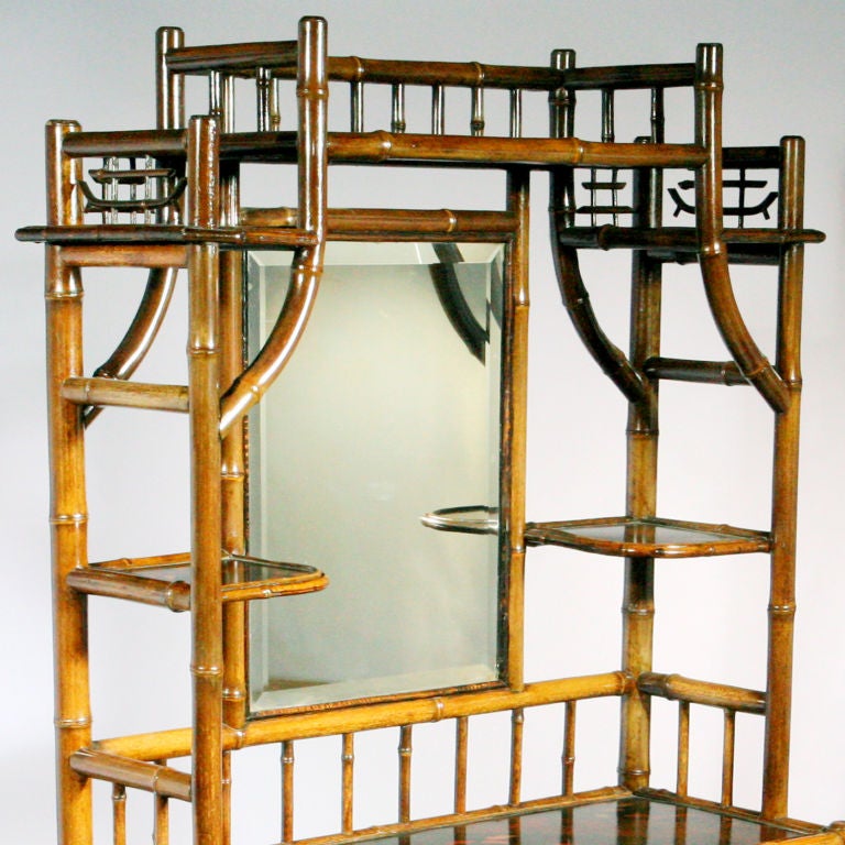 Impressive English bamboo hallstand or etagere with tiered top in Oriental pagoda shape.  Features center mirror framed by small display shelves and upper bamboo gallery.  Lower cabinet with wide upper and lower shelves, small center drawer, and
