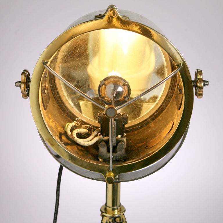Handsome turn-of-the-century British brass searchlight on polished white metal stand. Dial switches the beam from flood to spot light. Electrified and in working order.