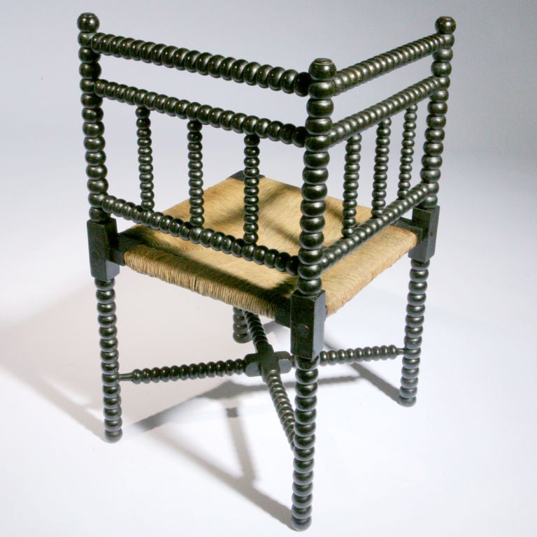 Striking antique English double-railed corner chair with Classic ebonized bobbin, turned legs and cross supports. Traditional patterned canned seat.