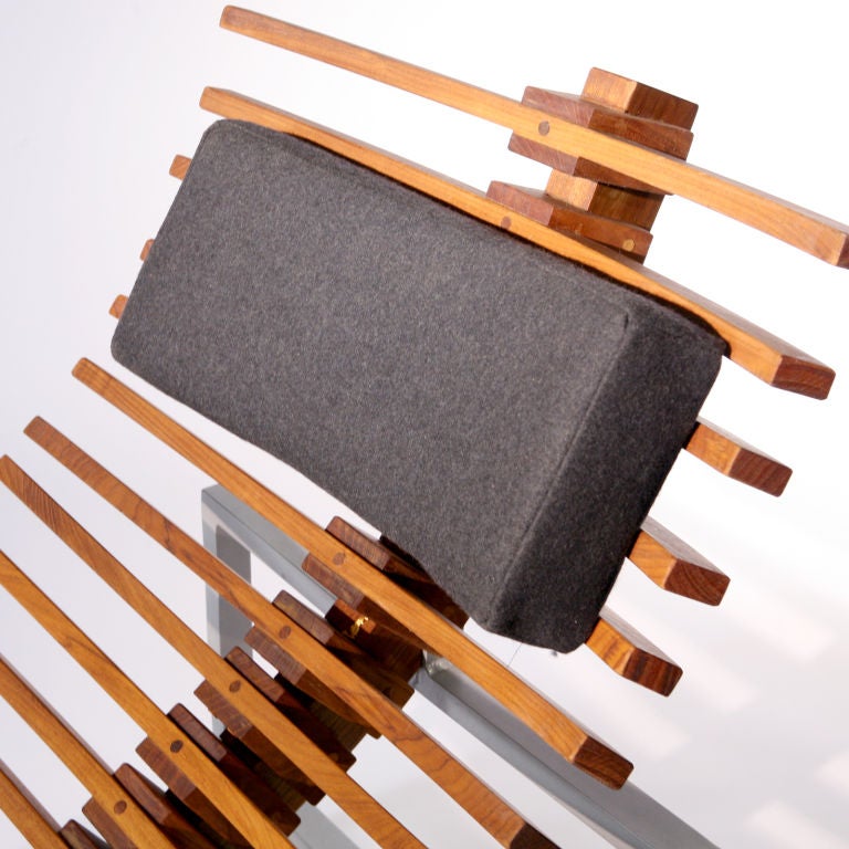 A slatted teak wood chaise on an aluminum frame with black cotton head cushion. Belgium design.