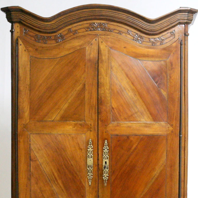 Early 19th century elegant French country armoire in a rich patinated cheerywood. Large chevron patterned doors, designed with shaped tops, mirror the double inverted dome that is set with deep- mouldings. Original brass hardware and old world