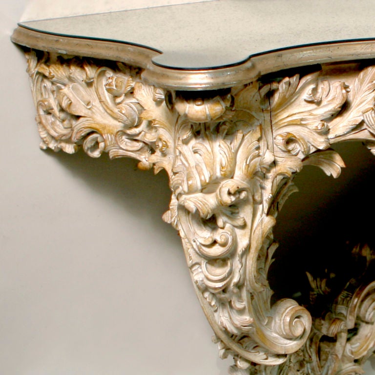 Pickled and bleached French wall console elaborately carved with scroll and flower pattern.  Beautifully detailed.  Shaped top refurbished with tinted, antiqued mirror.