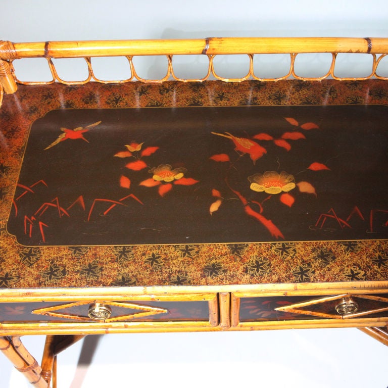 English bamboo writing desk with graceful bamboo topped gallery, two drawers, and a shaped lower shelf.  Beautifully painted in the traditional motifs of birds, flowers, and stripes in black, gold and orange chinoiserie.  Coordinates with our