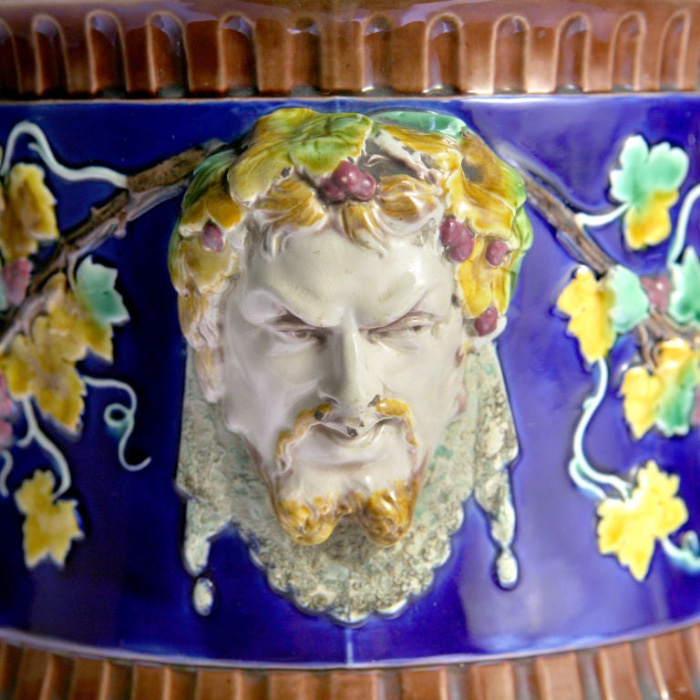 Pair of Wedgwood Majolica cache pots or wine coolers with strong Majolica colors of blue, yellow, green and brown. A grape and wine theme design decorated with clusters of grapes, grape vines and bearded Bacchus busts as handles. Impressed: