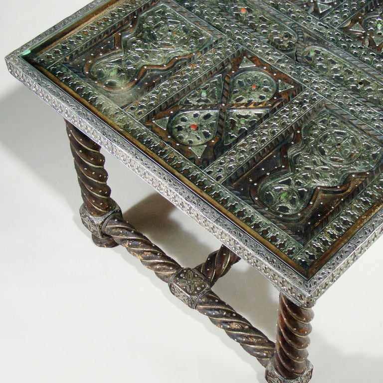 Intricately carved Berber tribe hardwood table with heavily patterned silver metal overlay and glass insert on large twisted legs with center stretcher. Tabletop and back of chairs designed with individually carved panels studded with semi-precious