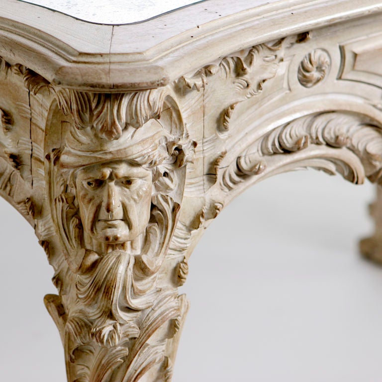Carved French center table with bleached and pickled finish and antiqued mirror top. This ornately carved wood table has beautiful details enhanced by the lighter finish. Carved with swirling leaves, flowers and mythological male masks on corner
