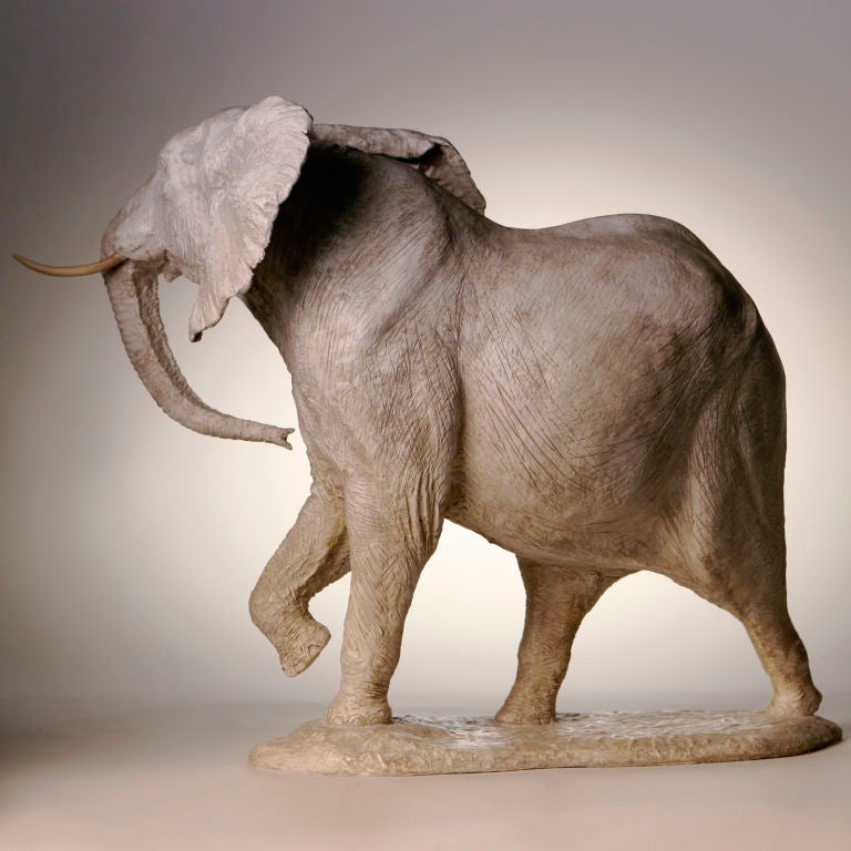 Magestic white plaster elephant with ivory tusks, trunk curled under and foot raised. By acclaimed French artist, Yves Gaumetou, known for animal sculptures that depict real life situations. Made in France in 1990.