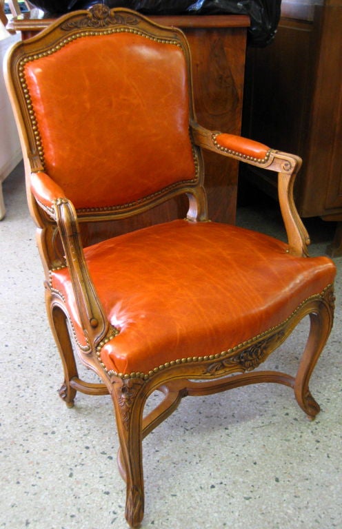 Beautiful pair of French Carved Fruit Wood Open Arm Bergeres/Armchairs. Upholstered in a rich leather with wonderful patina. Cabriole legs, great details in carving, beautiful patina on the frame, entretoise legs, wood peg technique, rich leather