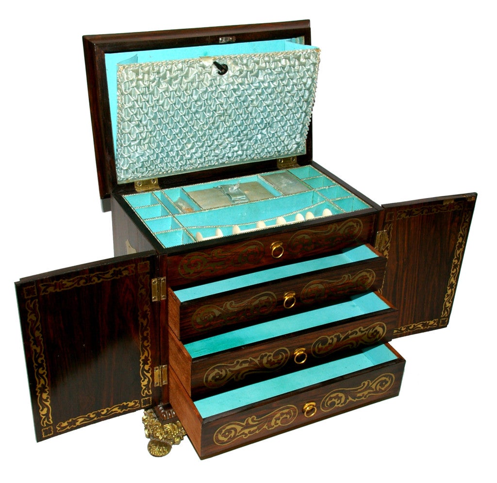 English Regency brass inlaid sewing box, c1810, rosewood with original silk interior raised on gilt brass feet. The top lifts to a divided interior lined in a blue paper and matching stitched fabric. The front with a pair of doors opening to three