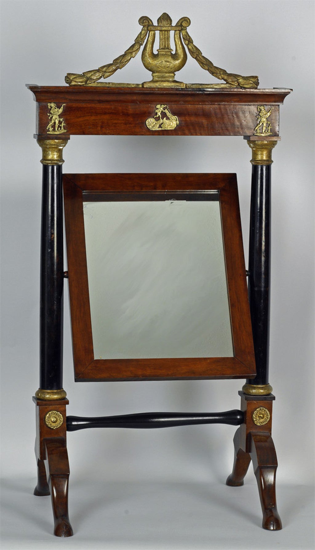 French Empire mahogany dressing table mirror, c1810, the case houses a “cheval style” mirror; it is surmounted by a gilt lyre and garland swag, the adjustable mirror is supported by ebonized columns, raised on a gilt brass-mounted trestle base.
N.P.