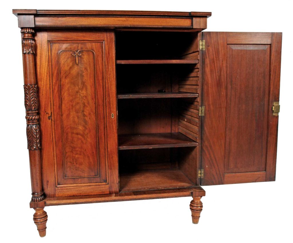 A Regency crotch mahogany two-door cabinet, circa 1810, the stepped reeded top over a pair of molded doors, opening to a adjustable shelved interior. The doors are flanked by turned and tapered acanthus carved columns; the whole raised on a molded