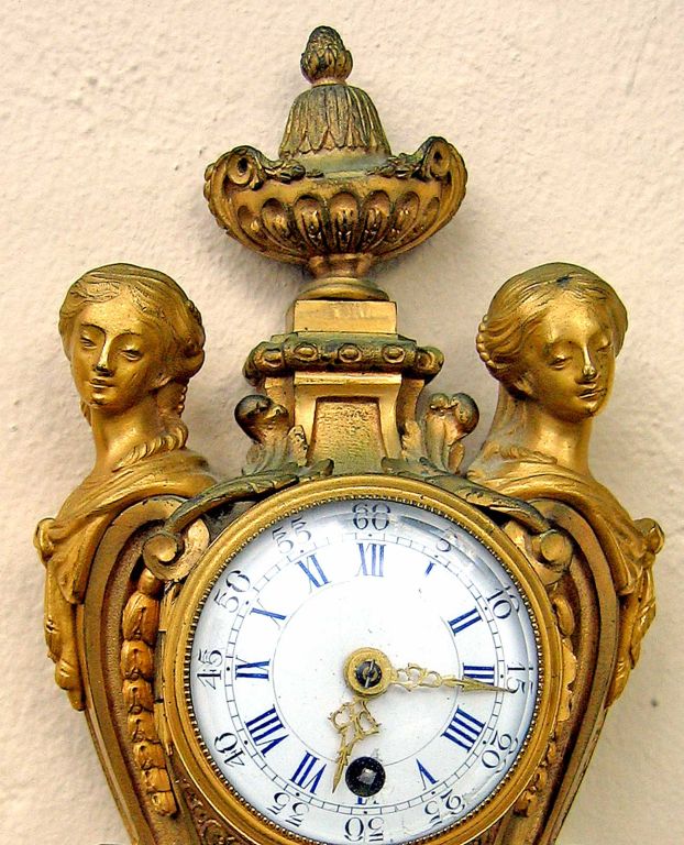 A Louis XVI Style ormolu Cartel clock, c1880, with a circular glazed enameled dial with both Roman and Arabic numbers, gilt hands, flanked by guilloche trailed herms and acanthus scrolls, the guilloche-molded front platform surmounted by a