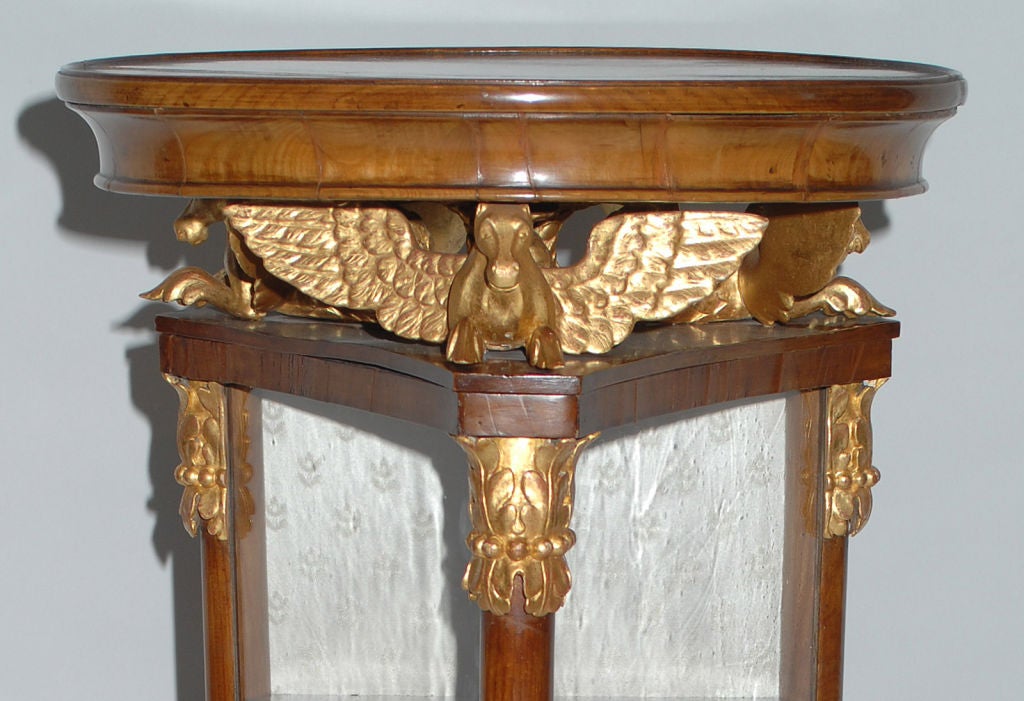 Triangulated Biedermeier cherry and gilt carved display cabinet c1830, with a circular top supported by three stylized, winged seahorses with five conforming wooden shelves raised on gilt decorated web feet above a conforming triangulated base with