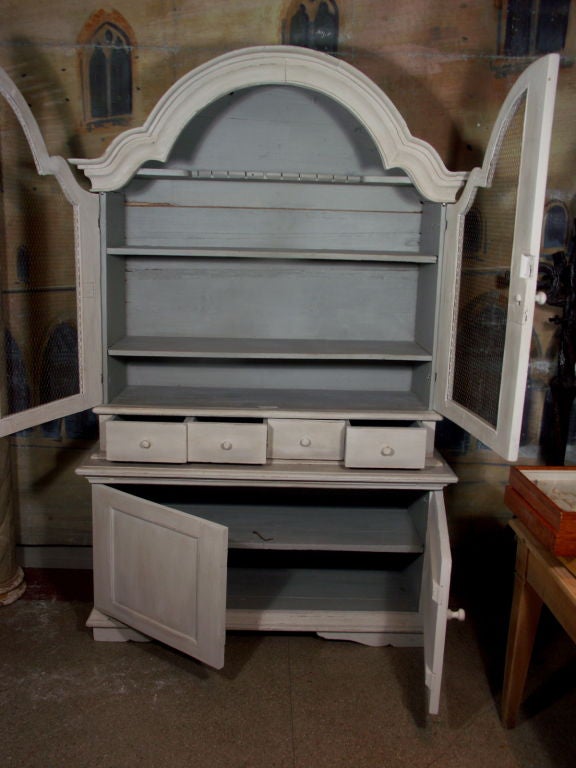 19th Century Painted Swedish Cabinet with 4 doors and 4 drawers.  Upper doors have open central panels completed with wire mesh grilles. Hand-forged iron strapped hinges on all doors.  Hand carving seen at crown of bonnet, feet, panels, and spoon