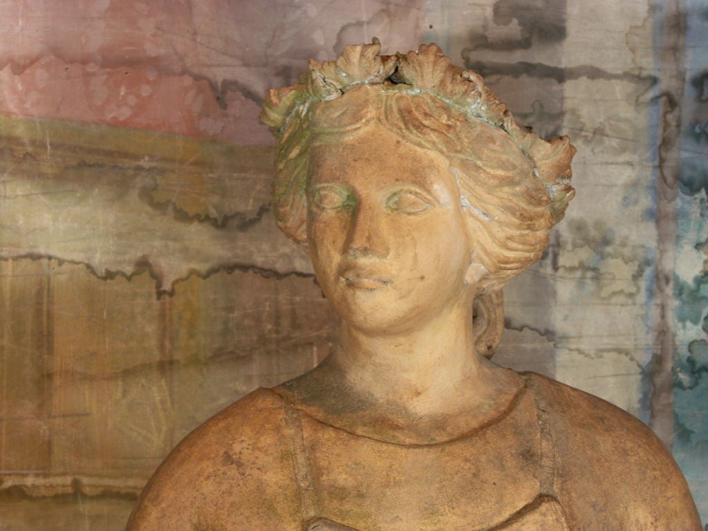 Terra cotta statue of girl holding grapes standing next to tree trunk, which projects 3