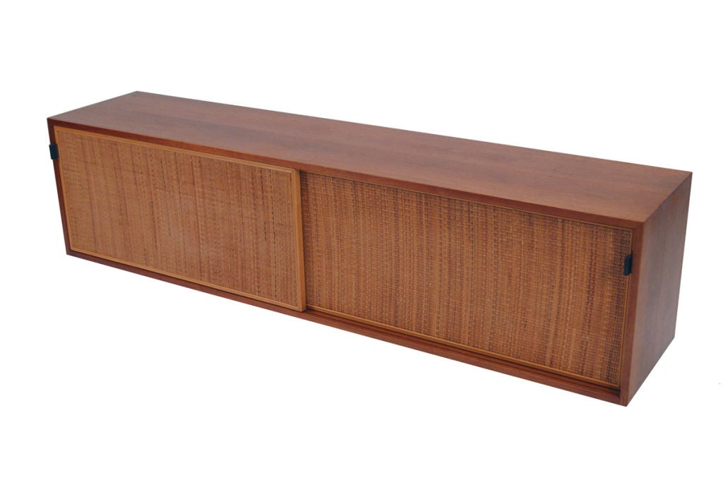 Hard to find Knoll wall hanging cabinet with sliding cane doors housed in a walnut case with leather tab pulls. Interior has adjustable shelves. Retains early Knoll label. Made by Knoll Associates