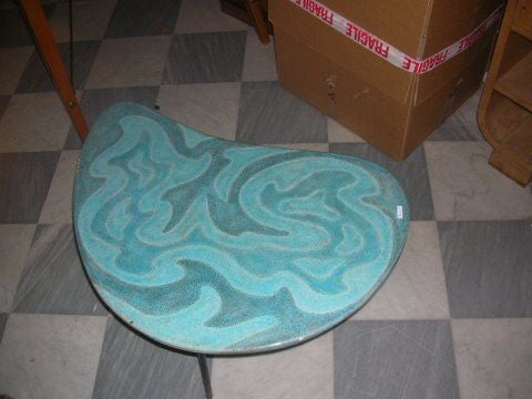 Table with blue/green ceramic boomerang-shaped top on three black.

Metal legs.