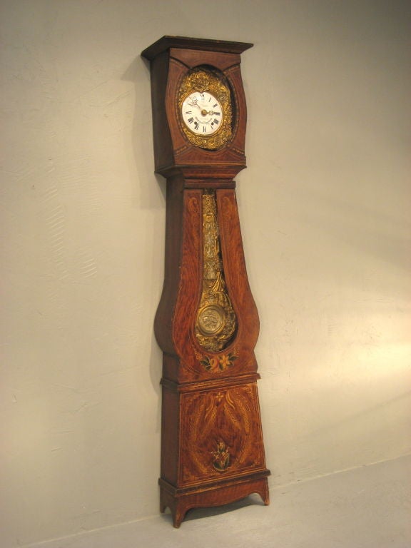 A Comtoise grandfather clock with a morbier movement, chimes on the hour, two minutes after and once on the half hour. A typical country clock with original painted pine case. The embossed pendulum is rich with floral detail and drapery as is the