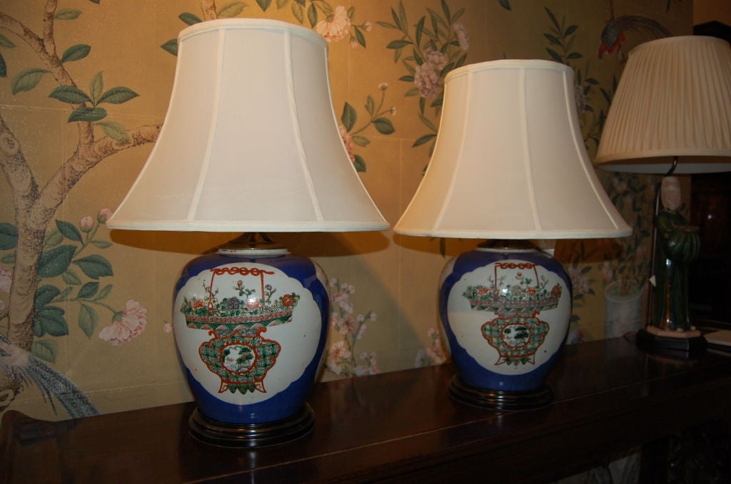 A pair of 19th century cobalt blue porcelain ginger jars.<br />
<br />
Drilled at base and mounted as lamps.<br />
<br />
Cobalt blue background with panels of design in famille verte tones.<br />
<br />
Design of baskets full of flowers,