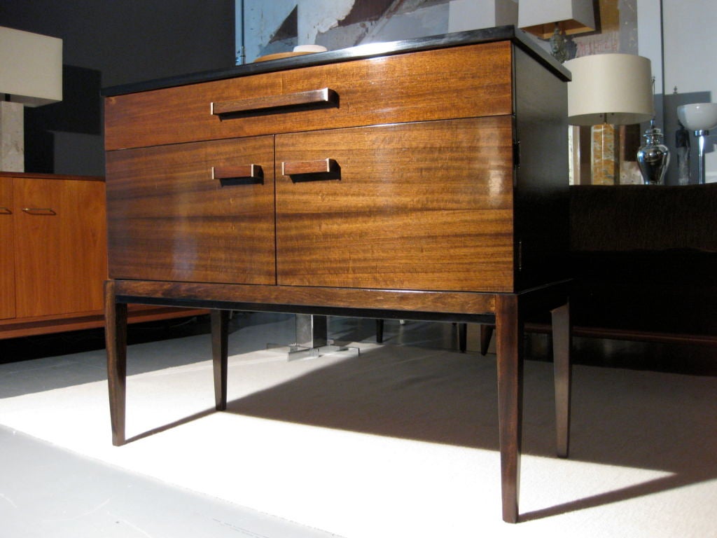 Art Deco sideboard of tiger mahogany designed by Donald Deskey for AMODEC in 1931. Beautiful proportions on tall tapered legs. One long drawer with dividers and two cabinet doors with wooden handles with thick square brass caps. Reminiscent of case