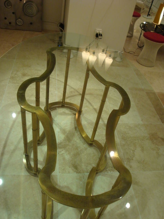 A oval dining table featuring a brass base with four sets of three legs and an original thick glass top. By Mastercraft, 1972. The table comes with documentation.
