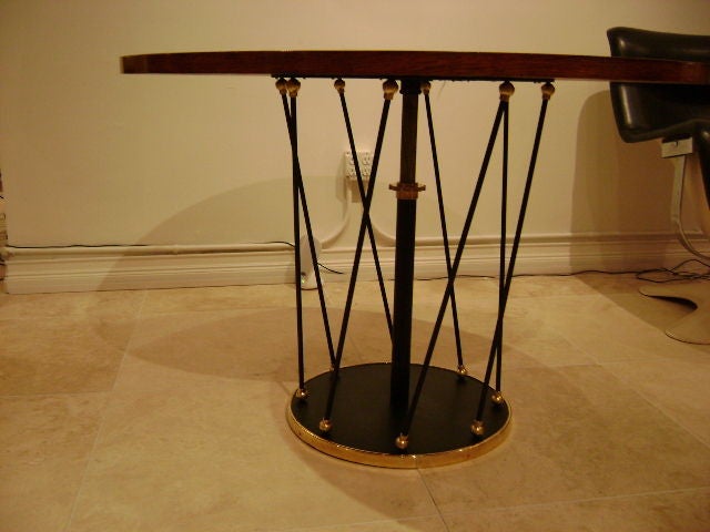 A round table featuring a quartered Oak veneered top with a round base in black lacquered metal edged in brass. The table top is held up via a center rod with multiple black lacquered metal rod and brass spheres along the bases edge. The table has