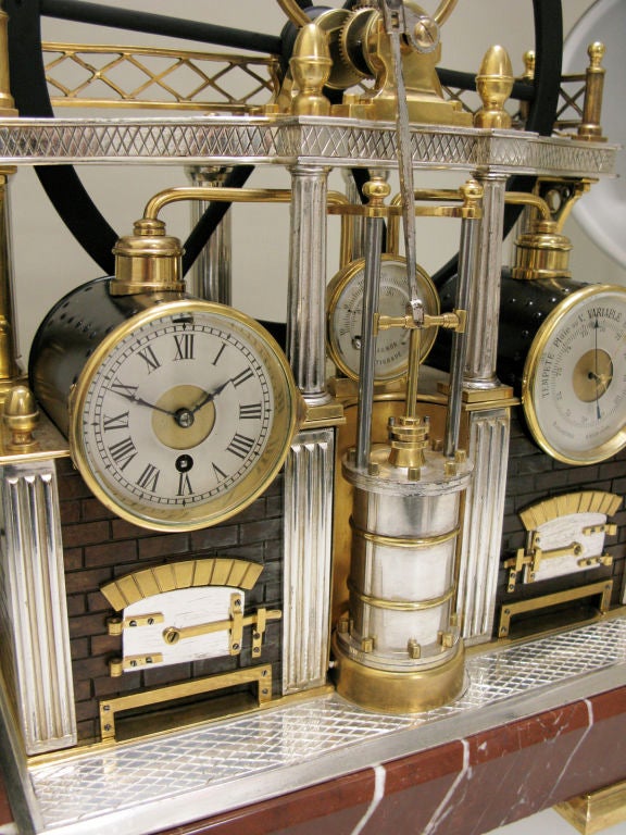 A good French industrial series gilt and silvered brass miniature steam-engine form weather station with a large flywheel and piston, the brickwork furnaces housing the timepiece and barometer in drums flanking a central thermometer, raised on rouge