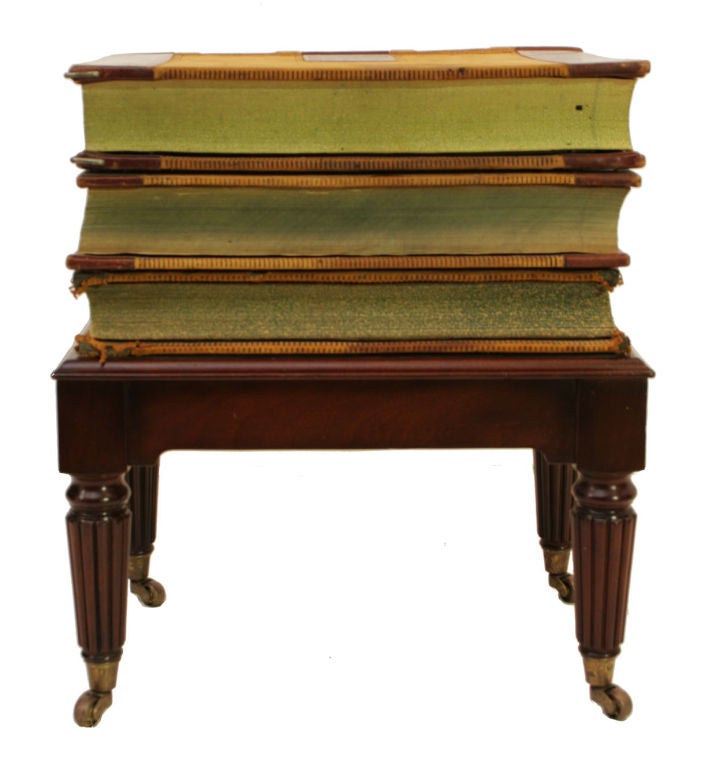 A side table composed of three antique leather-bound ledgers stacked on a Regency style mahogany base ending in casters.