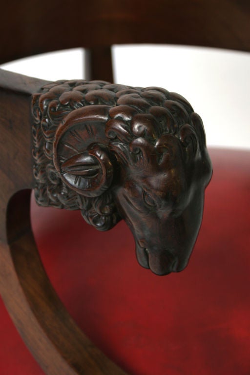 Fine Empire mahogany library tub chair, the broad top-rail with well-carved ram's head terminals on downswept supports, with <br />
bullseye roundels heading the turned legs