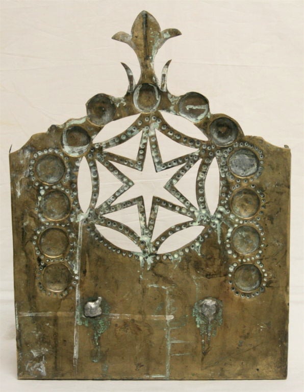 This is a beautiful and quite rare Dutch menorah from the early 18th century. It is made of hand hammered traced and punched brass. The shelf that covers the oil holders lifts up so that it can be lit. The shammos is removable, and attaches to a peg
