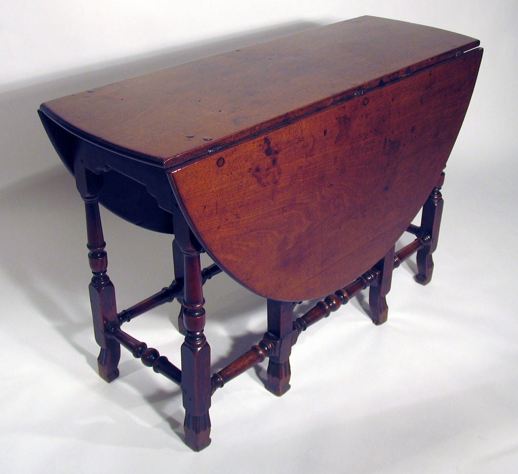 Circa 1700. An oval top with drop ends is supported by two “gate legs” with baluster-turned supports, joined by turned stretchers; raised on rollover trefid feet.