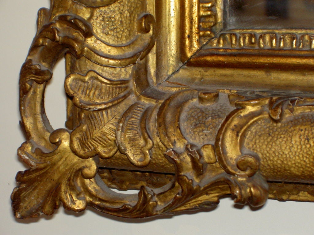 Carved and gilded, with mirrored pediment of scrolls headed by a shell, the sides with foliate pendants, re-placed glass<br />
With Adolph Loewi, Venice, Italy and Los Angeles
