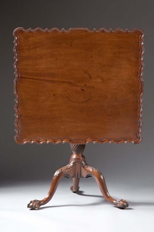 A Chippendale carved mahogany silver/tea table with a rectangular single board tilting top with pie crust carved edge, fluted and spiral turned shaft, tripod base with ball and claw feet, English, Circa 1750. A closely related example is in the