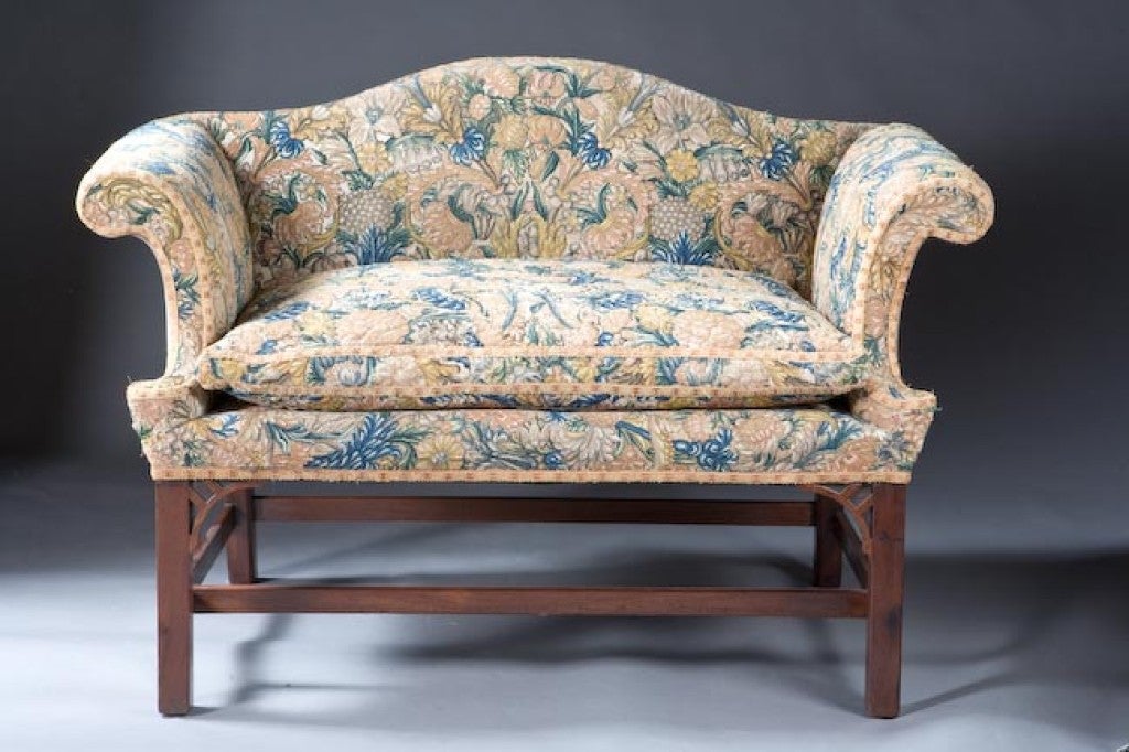 A George II needlepoint covered small scaled Chippendale camelback settee with marlborough legs in mahogany. The period needlepoint with floral decoration is on a traditional camel back settee frame with rolled arms. The four legs are joined by an