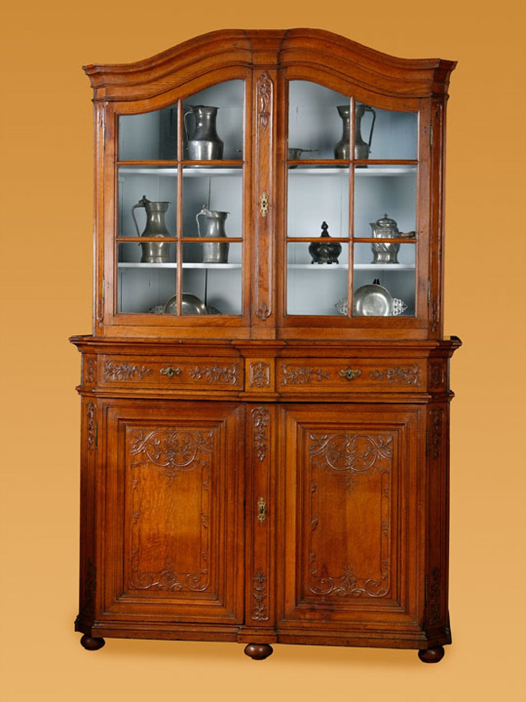 French provincial Louis XVI oak vitrine, with flower carving

in two parts the shaped top with two glazed doors for display

the base with two drawers over two doors on turned ball feet
