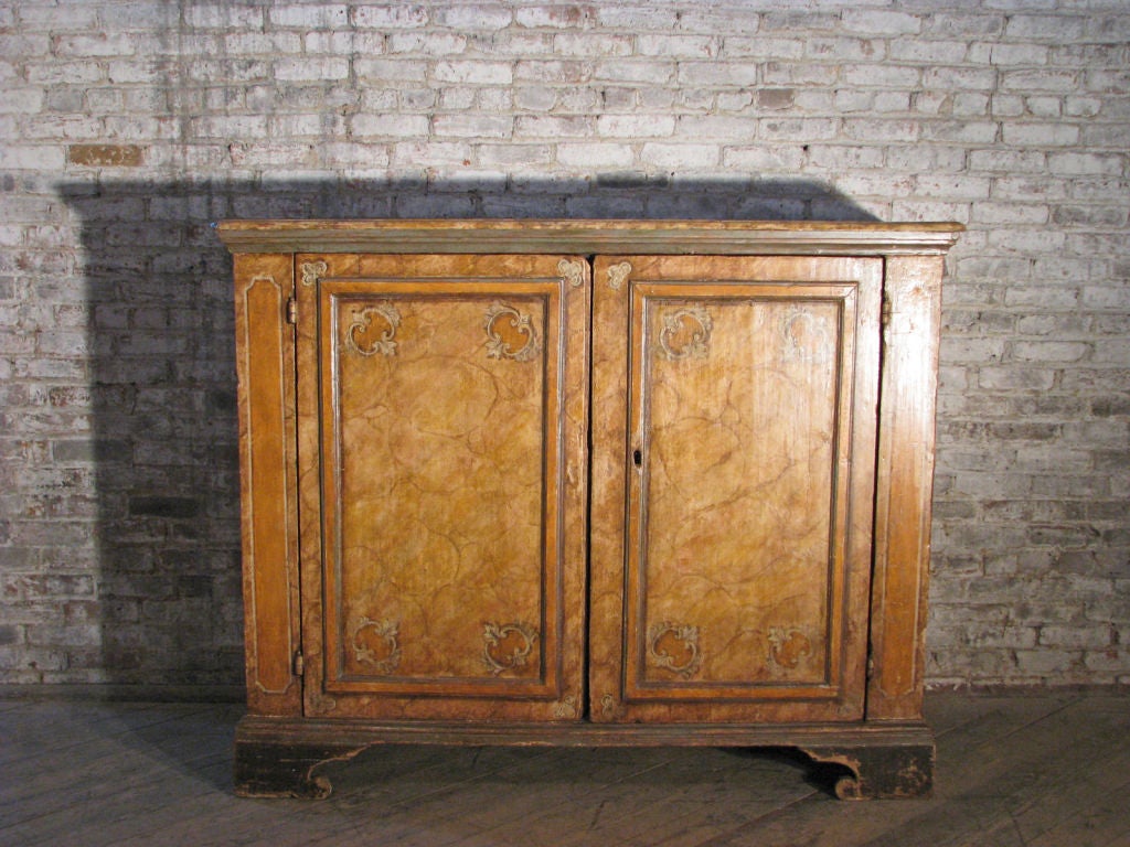 Finely executed and high quality baroque two-door cabinet/credenza, painted in cheerful yellow hues to simulate marble, interior with fitted with one shelf.
