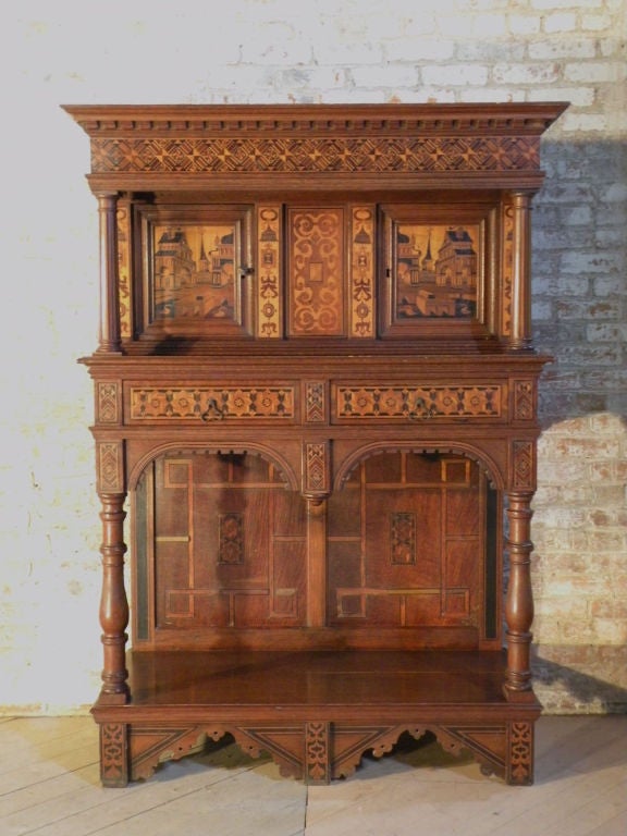 Very decorative inlaid cabinet. The upper part containing two doors, inlaid with architectural trompe-l'oeil of imaginary towns, two drawers, open lower section. Overall decorated with geometric and floral inlay of various woods.
