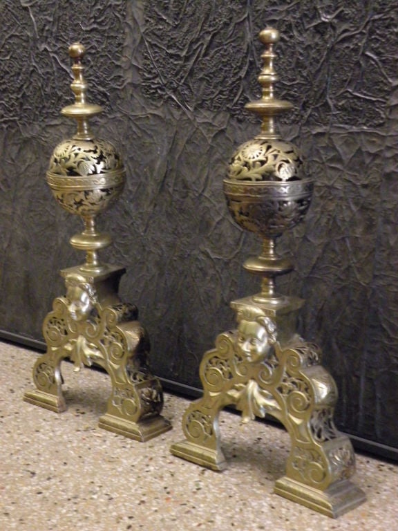 Pair of decorative brass andirons of Baroque style, the pierced scrolled base, centering a female mask, surmounted by a conforming pierced bowl, topped by a turned finial.
Missing the iron log supports.
