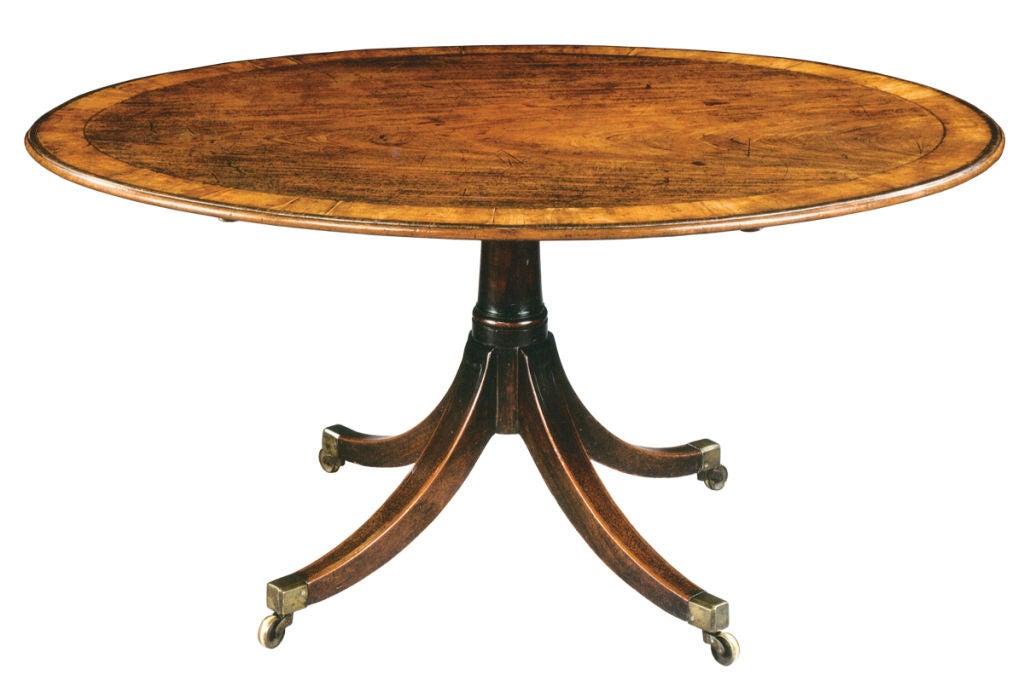 An English oval breakfast table with exceptional color and surface. The highly figured mahogany top is bordered by a wide strip of cross-banding bordered on both sides by stringing inlay and surrounded by a thinner strip of cross-banding. The four