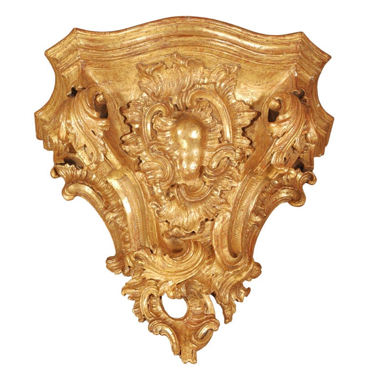 A pair of large-scale gilded brackets carved with a central cabochon surrounded by flowing acanthus leaves and interlocking C-scrolls. The top has a conforming molded edge and serpentine-shaped front. Large enough to use as a pair of console tables.