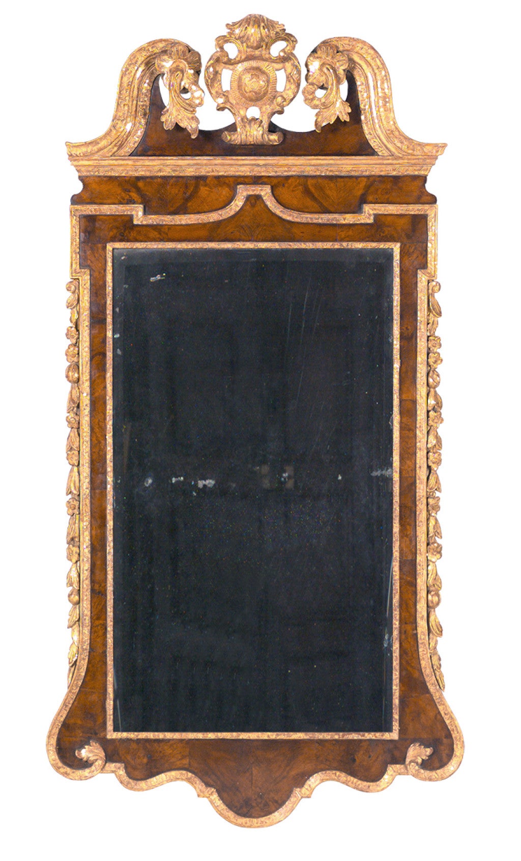 A large walnut veneered and parcel gilt mirror. The swan neck pediment is centered by a shield cartouche. With the original, beveled mirror plate.