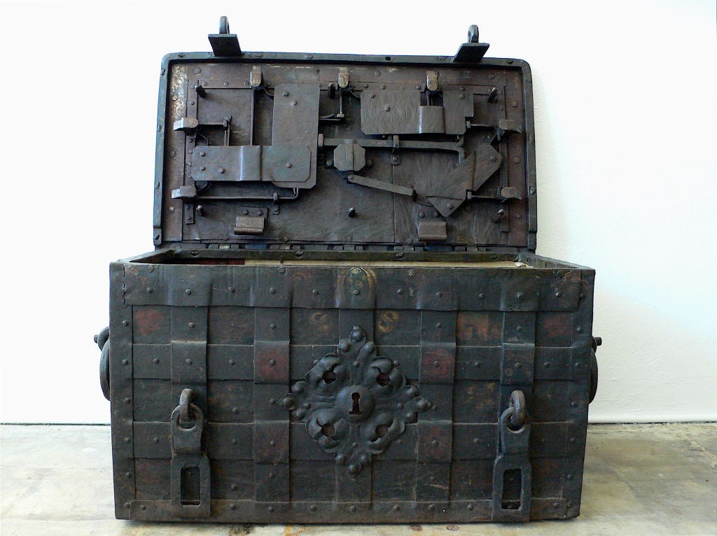 Painted iron chest bound with iron straps with hasps and pierced false escutcheon and twin writhen handles. Top key turns an elaborate locking mechanism, with pierced foliate engraved steel plate, shooting nine bolts to the interior. A second iron