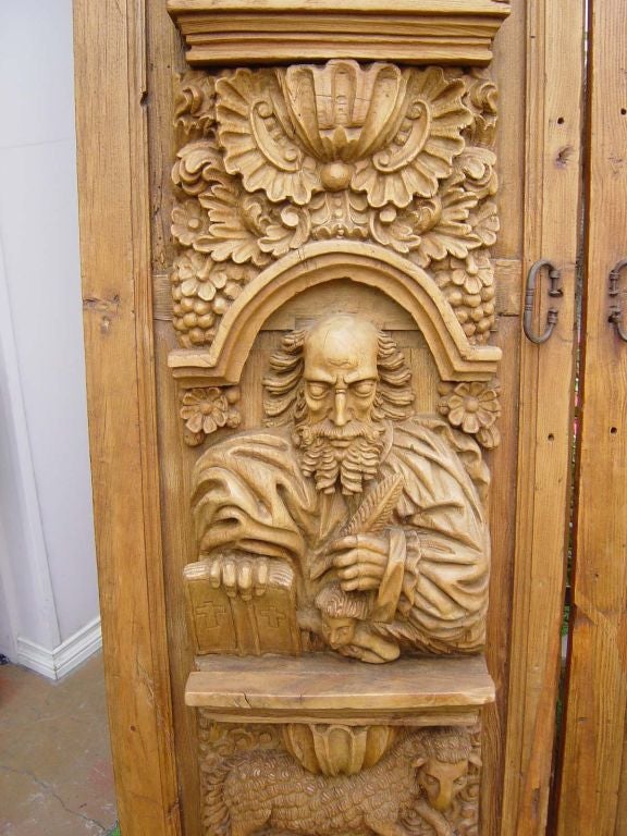 A pair of heavily carved wooden doors with motifs of the Four Evangelists shown with their symbols under their arms and also a pascal lamb and angels heads.  The backs of simple panel form. Retaining their original forged iron pulls.  These doors