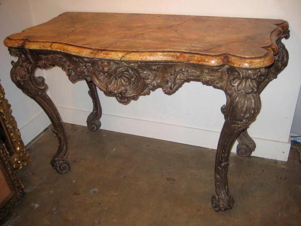 Large hand carved, turn-of-the-century, wood console from Florence, Italy. The richly carved, silver gilt body is adorned with beautiful shell reliefs and terminates in cabriole legs. Surmounted by a hand painted faux marble top,.