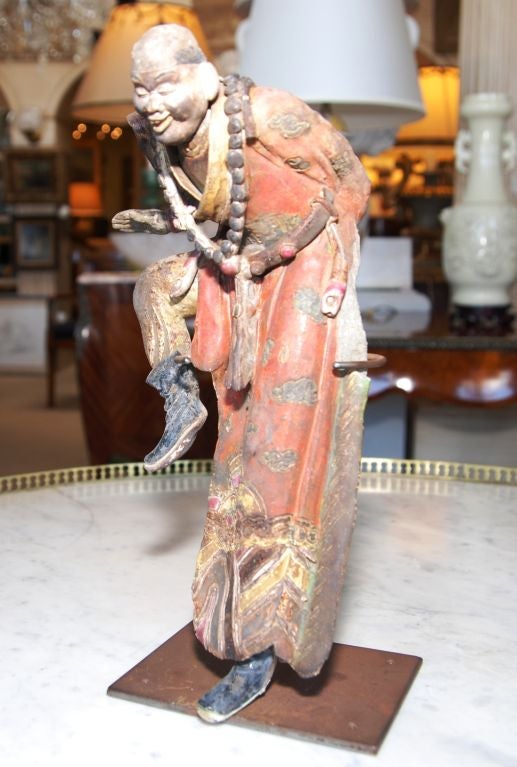 A very whimsical figure of a dancing man in robes as a Chinese glazed terracotta roof tile. He has beads around his neck, a tasseled belt and boots on. These tiles were used for good luck and as talismans to ward off evil. The tile is displayed on